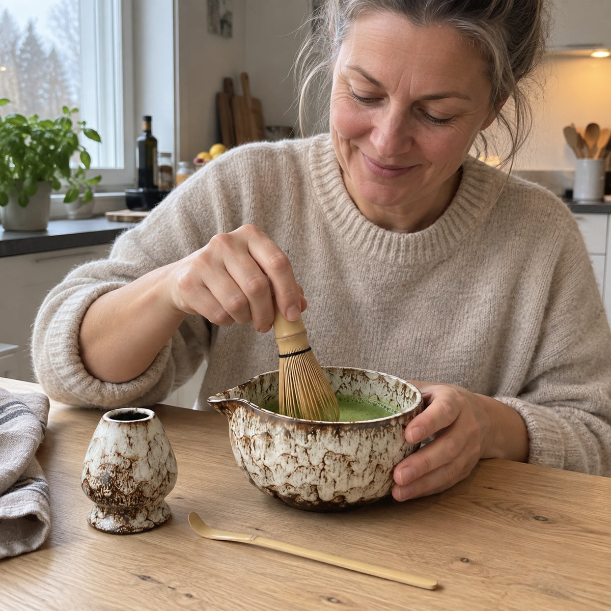 Kvinne visper matcha i Mossa-skålen ved kjøkkenbordet