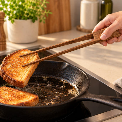 Teak wooden tongs lifting a slice of fried bread from a frying pan
