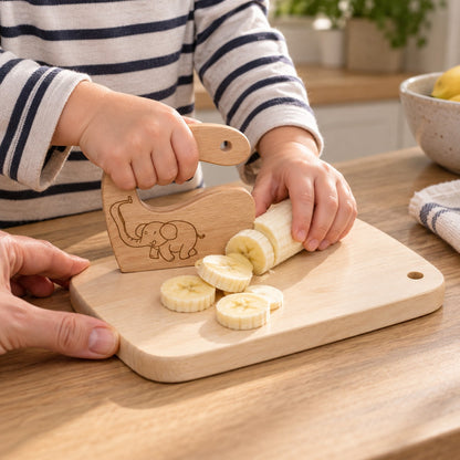 Children's hands cutting a banana with the safe wooden elephant knife on the chopping board from the kitchen set