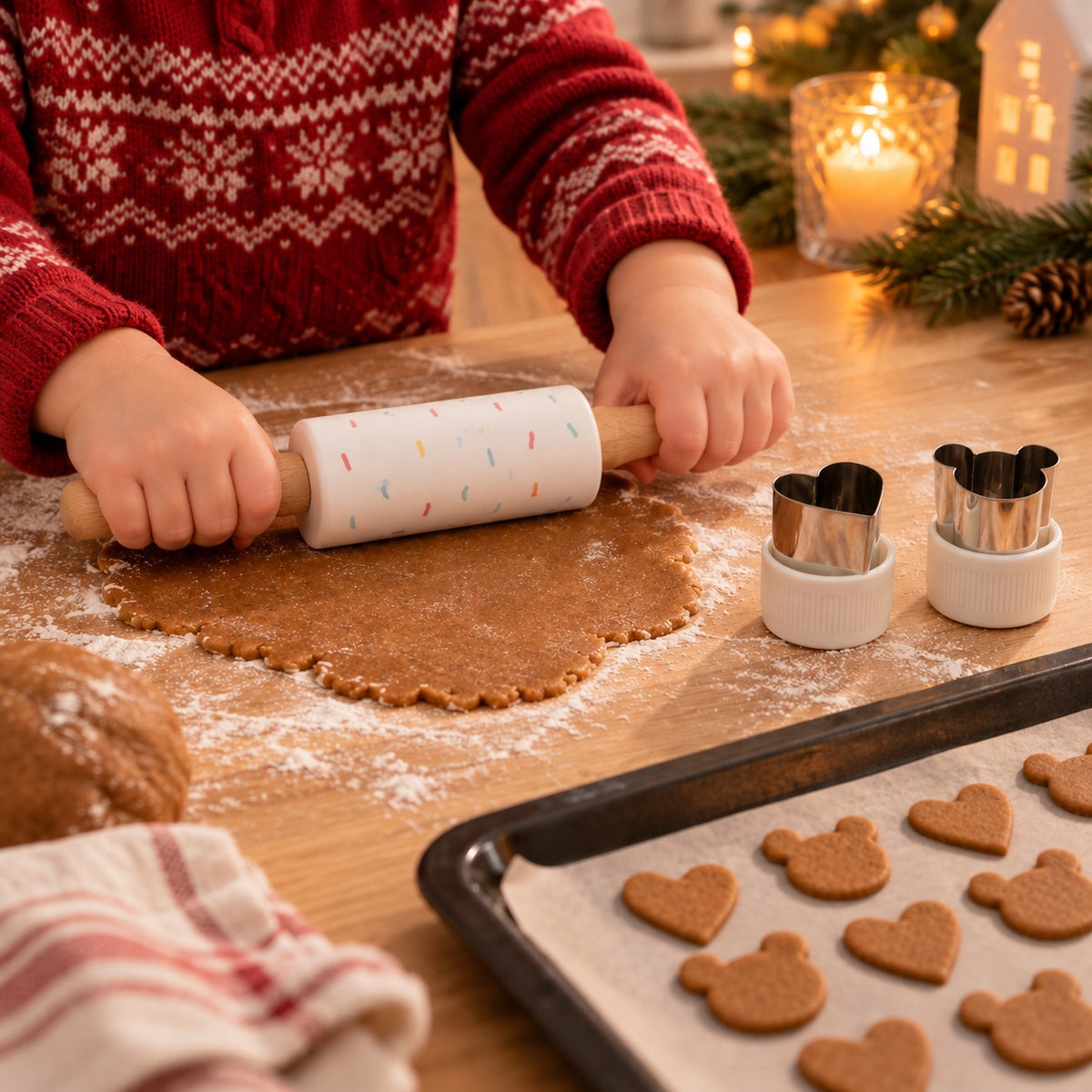 A child rolling out gingerbread dough with the small rolling pin, with the heart and teddy bear cutters from the set beside it