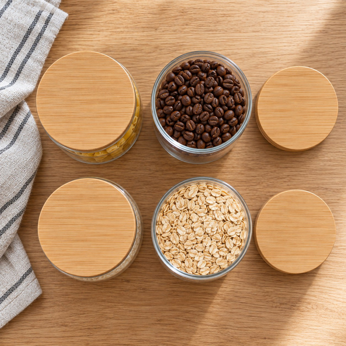 Four glass jars with bamboo lids viewed from above, two open and containing coffee beans and rolled oats