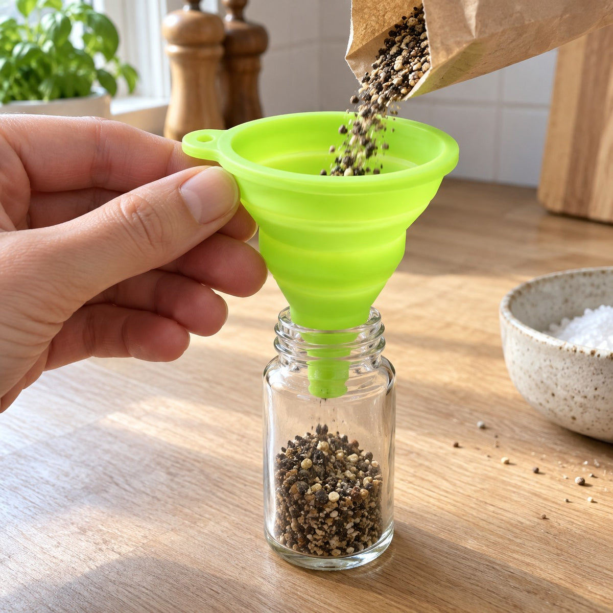 Hånd holder silikontrakten over et krydderglass mens pepper fylles på